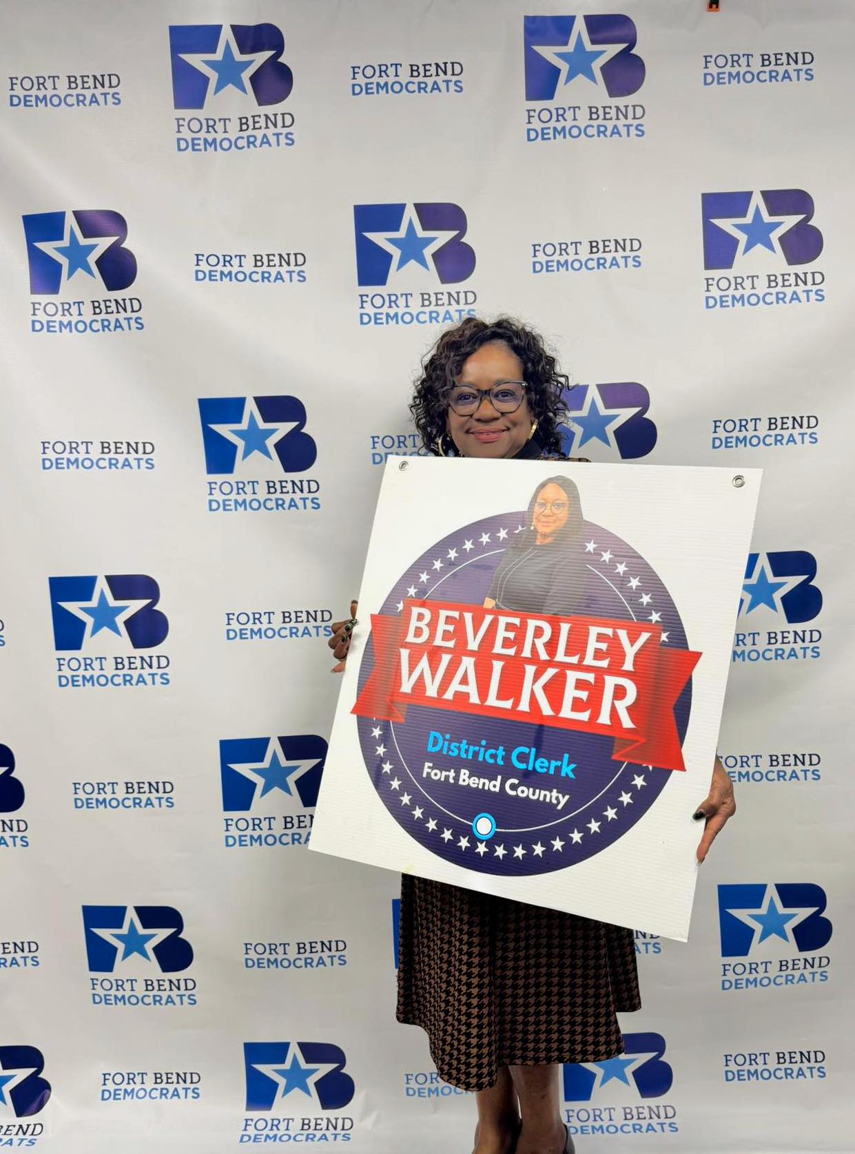Mujer sosteniendo un cartel de campaña de Beverley Walker, candidata a secretaria de distrito, con fondo de logotipos de Fort Bend Democrats.