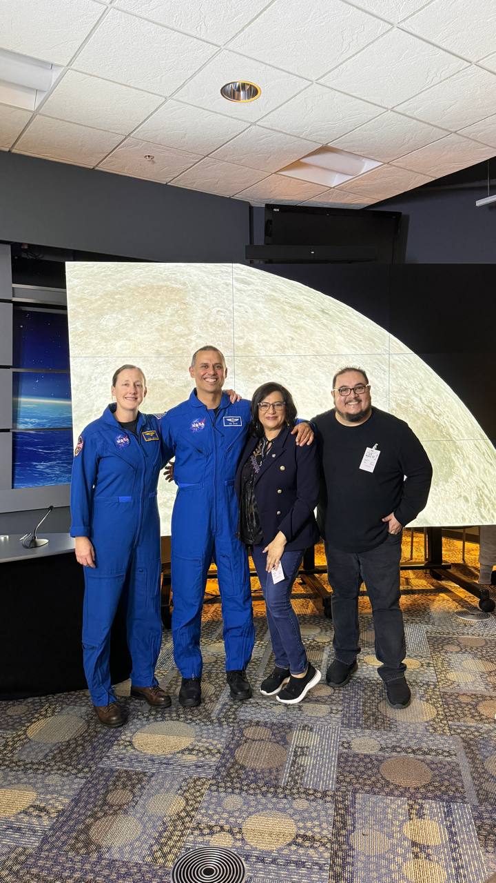 Daysi Marin y Mauricio Marin, directores de Se Habla Español News, con dos astronautas frente a pantalla de la Luna en el Johnson Space Center