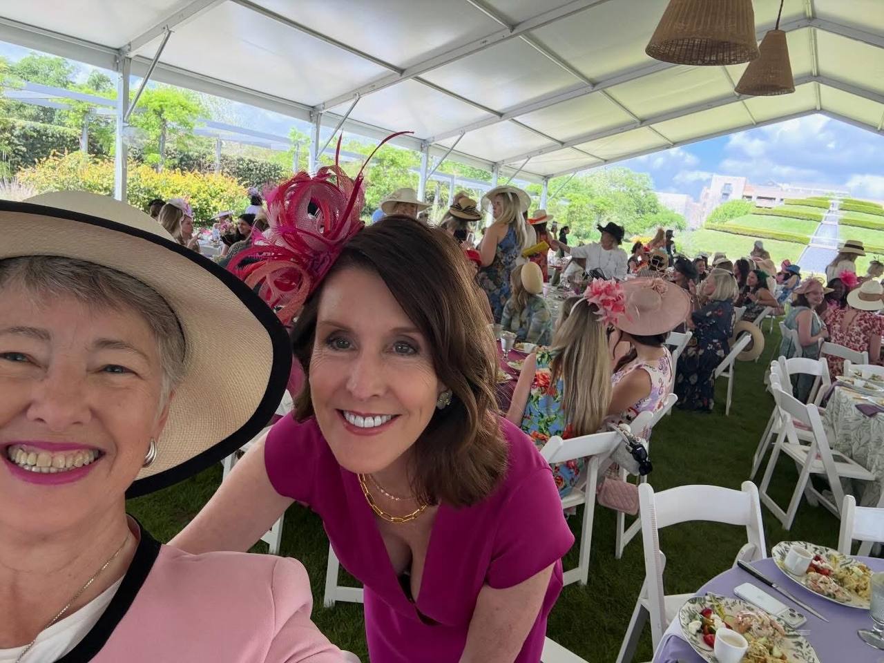 Annise Parker selfie con asistente en vestido fucsia en The Hats in the Park Gala con mesas y asistentes al fondo