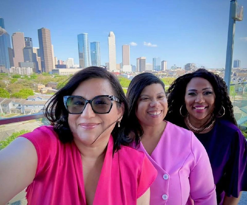 Selfie de Daysi Marin (blusa rosa) con dos mujeres líderes con skyline de Houston de fondo