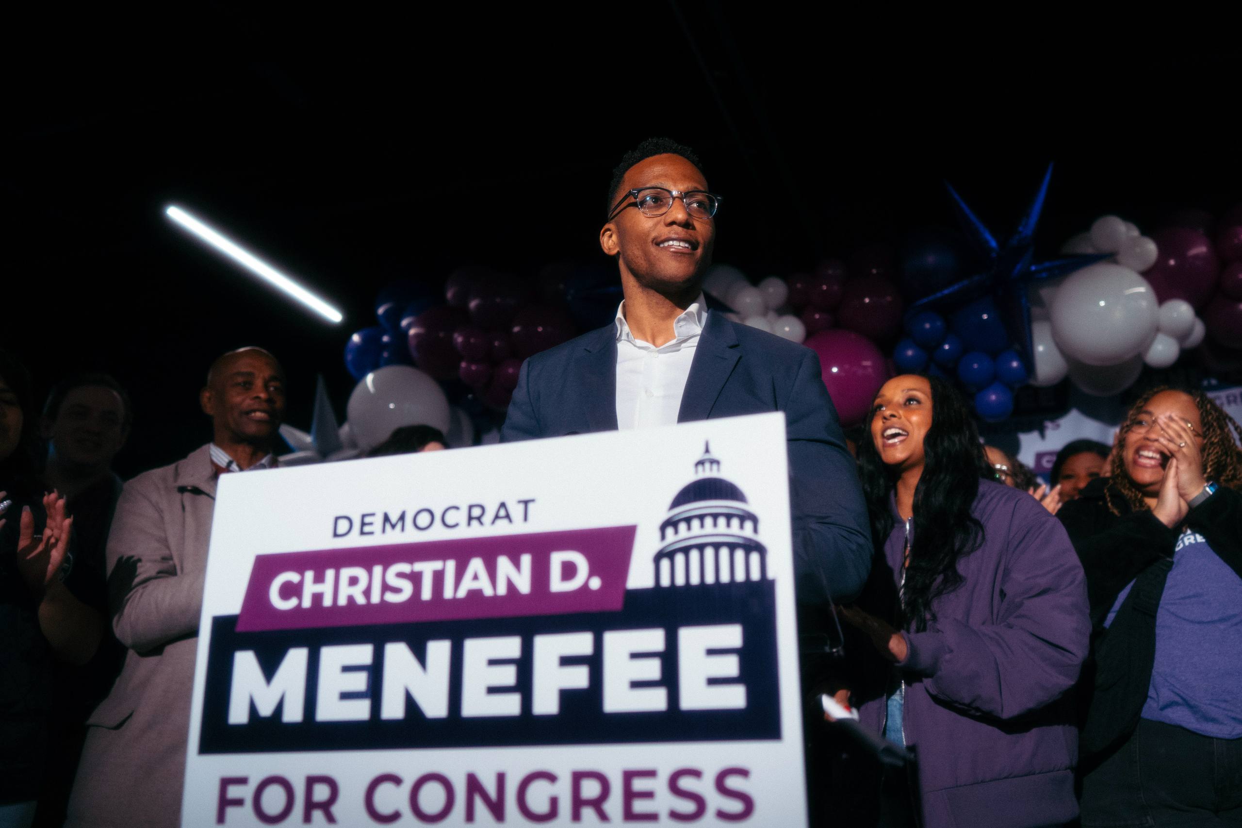 Christian Menefee celebrando en la noche de elecciones con cartel Democrat Menefee For Congress