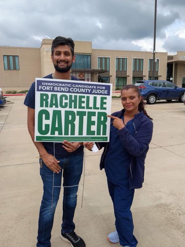 Pareja joven sosteniendo letrero de Rachelle Carter candidata democratica para Fort Bend County Judge