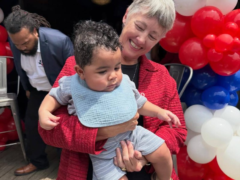 Annise Parker sonriendo mientras sostiene un bebé durante el evento Houston Voting Initiative